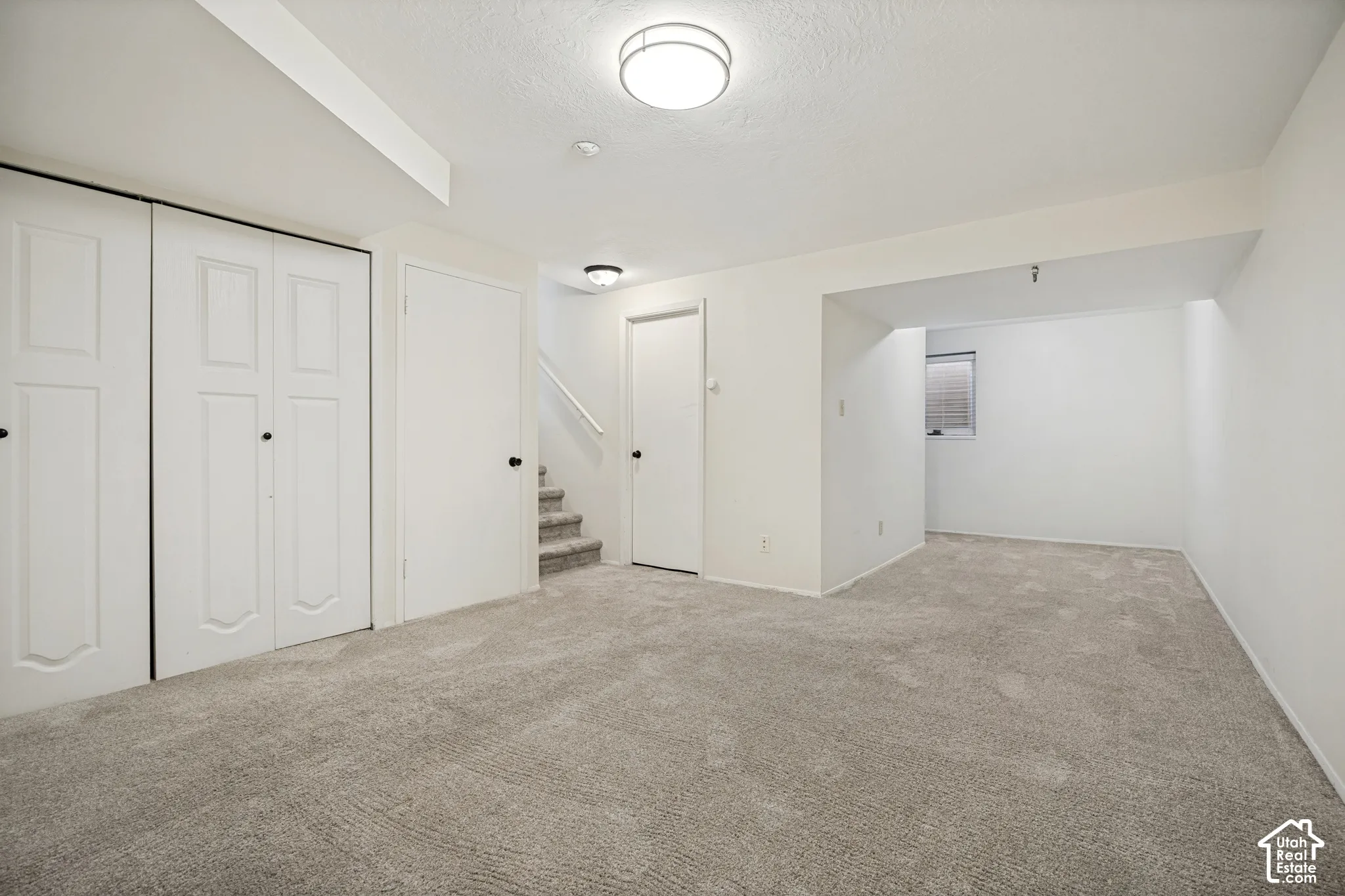Interior space featuring neutral wall-to-wall carpeting, recessed and surface-mount flush ceiling lighting, white dual-panel closet doors, and a staircase with wall-mounted railing