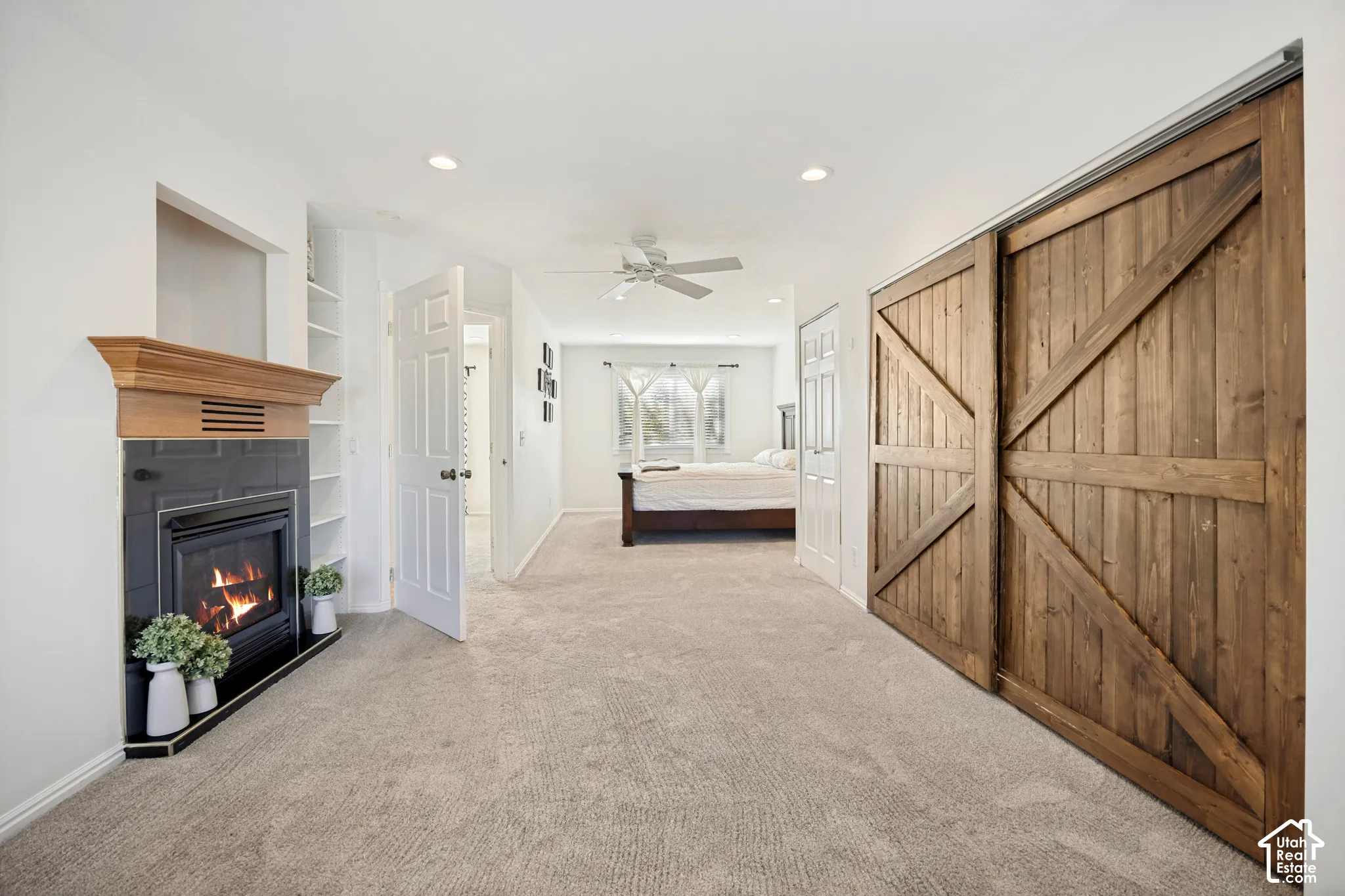 Fireplace with a black tile surround and wood mantel, sliding wood barn doors, recessed ceiling lighting, and a ceiling fan