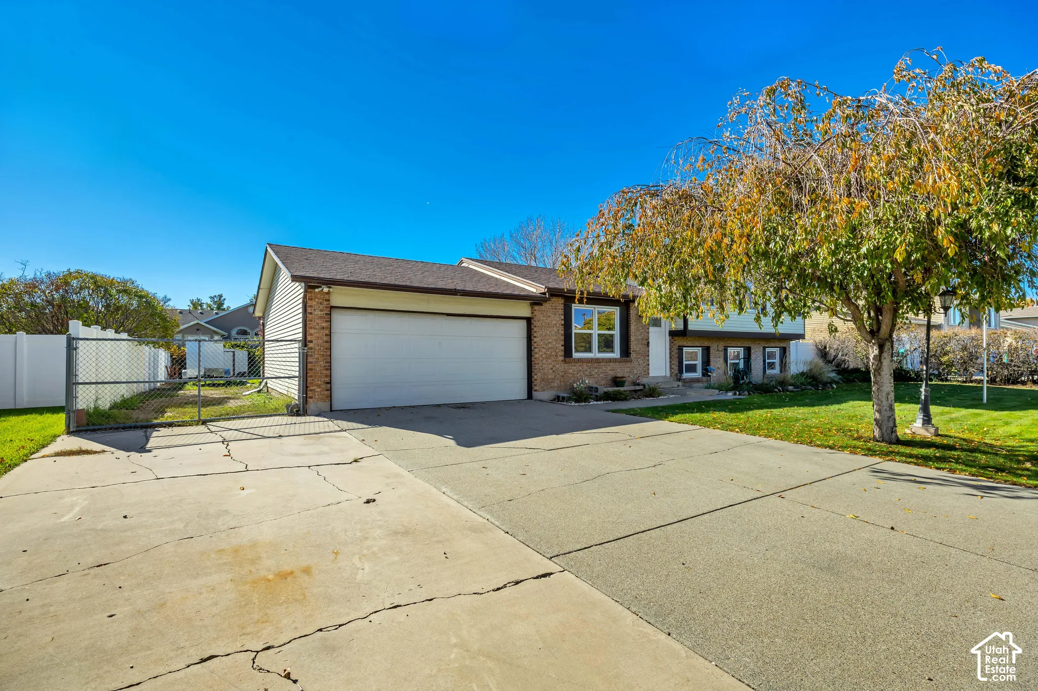 Single-story exterior featuring a brick and siding facade, attached two-car garage, concrete driveway, and white vinyl privacy fencing