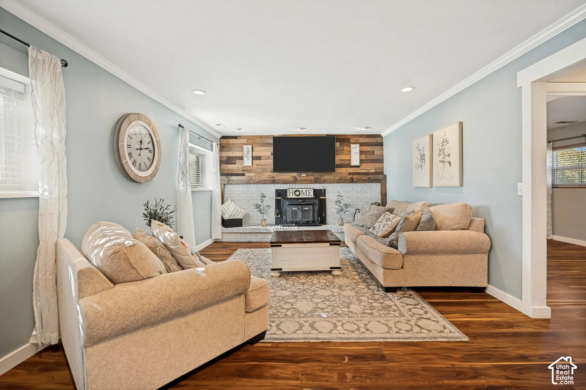 Living area featuring wood-finish flooring, white-painted brick fireplace, and accent wall with horizontal wood planks