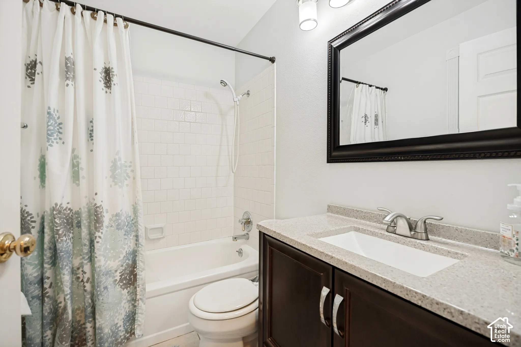 Bathroom featuring a vanity with a stone-composite countertop, integrated sink, dark wood-finish cabinetry, framed vanity mirror, and a tub-shower combination with subway-style wall tiling