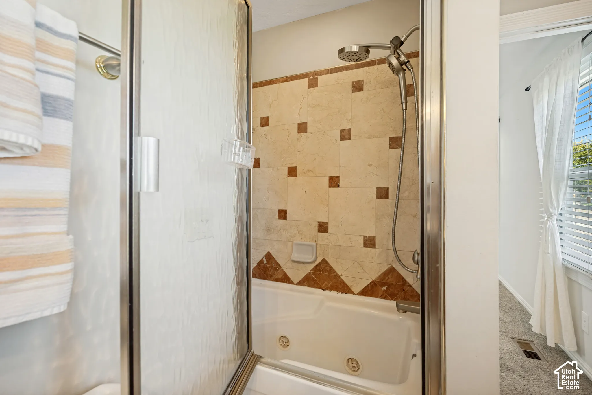 Jetted soaking tub featuring tile surround with decorative stone inlays, framed glass shower enclosure, and handheld shower fixture