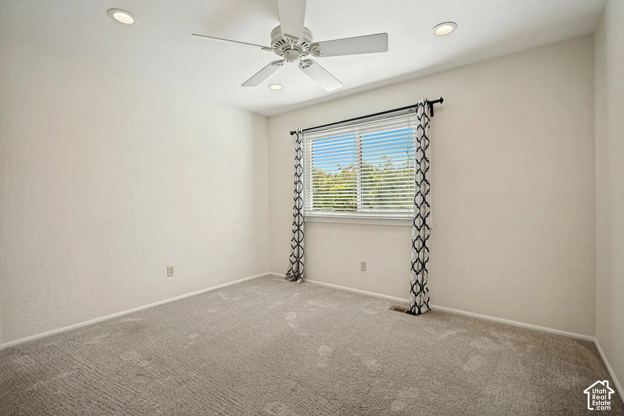 Neutral-toned carpeted room featuring a ceiling fan, recessed lighting, and a single window with blinds