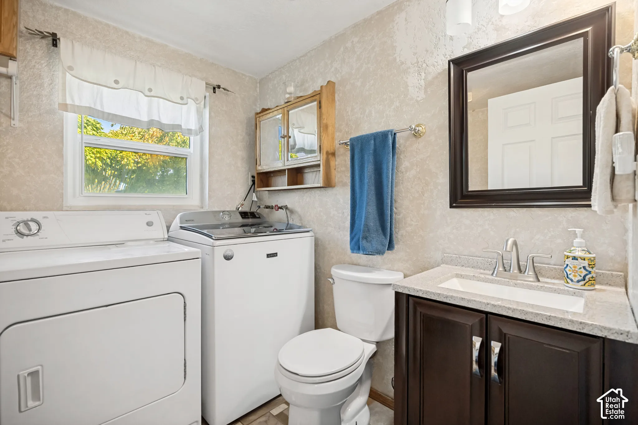 Bathroom featuring a vanity with dark-finish cabinetry, light-toned stone-finish countertop, integrated rectangular sink, and polished metal hardware, paired with a wall-mounted wooden cabinet