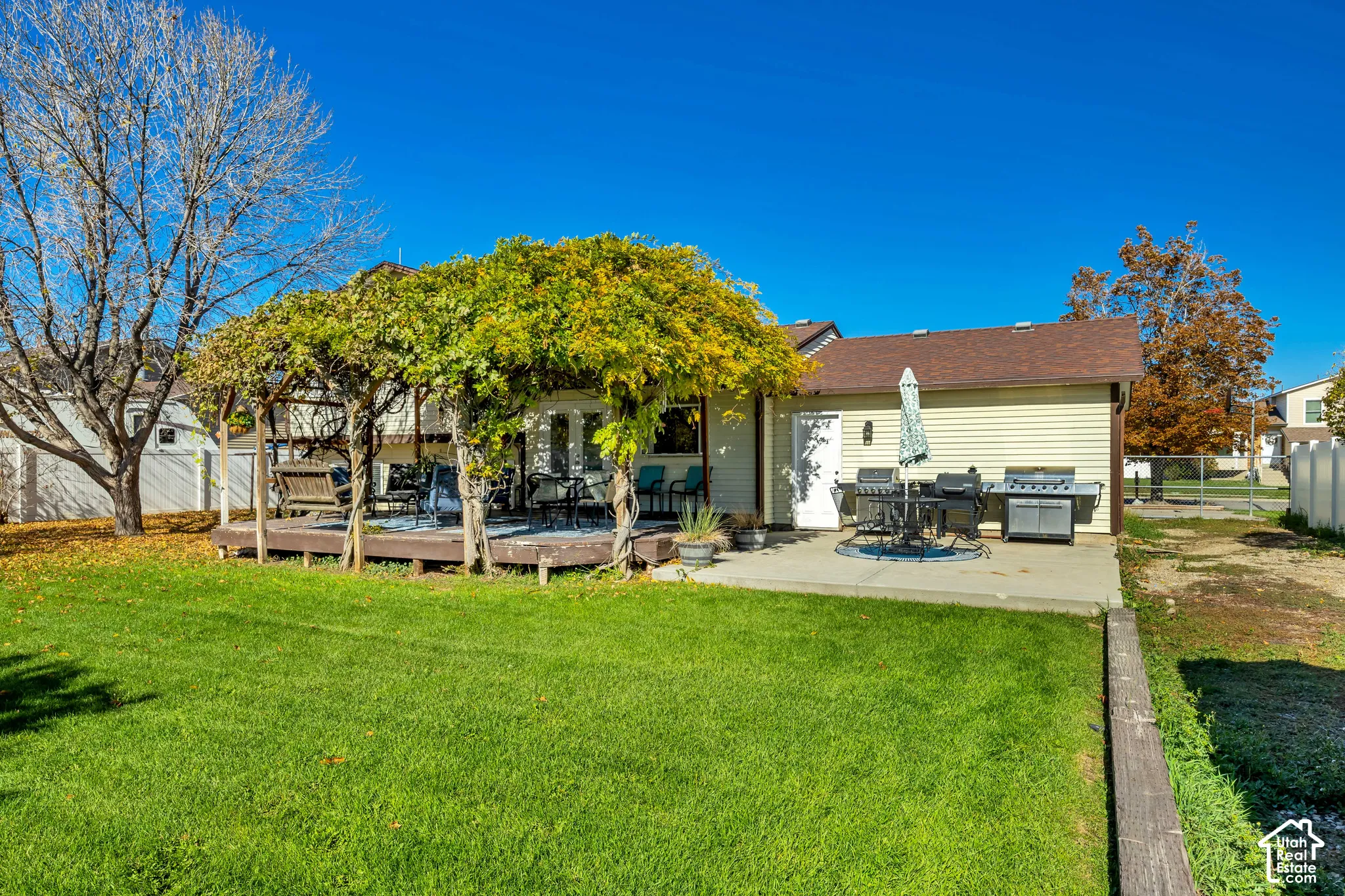 Backyard featuring a wood-decked patio with a covered pergola, a concrete patio area, and a lawn