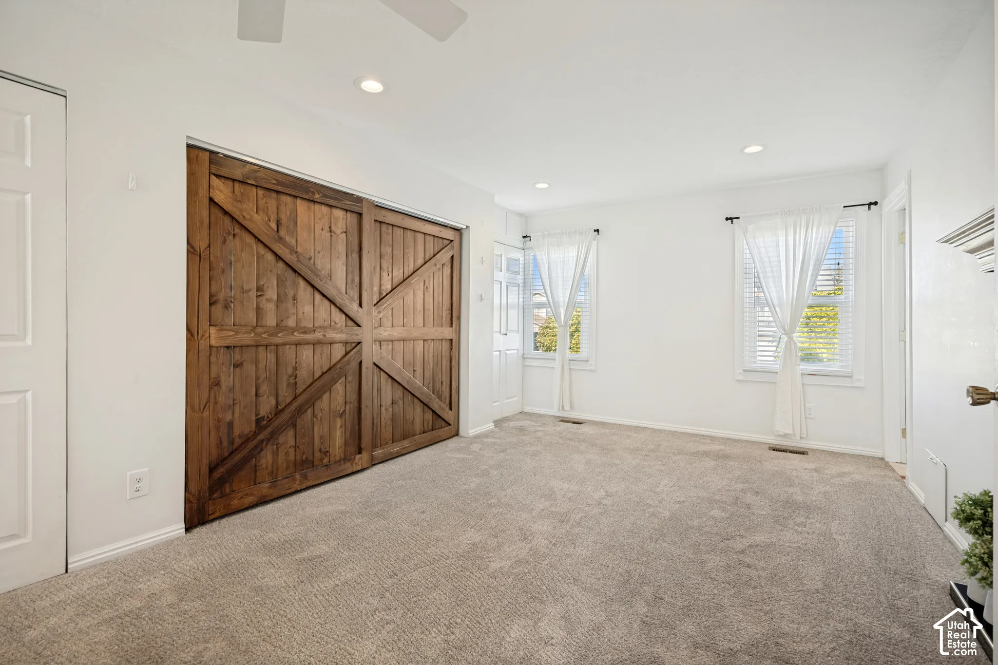 Interior room featuring oversized wood-finish sliding barn doors, neutral wall-to-wall carpeting, recessed ceiling lighting, and dual windows