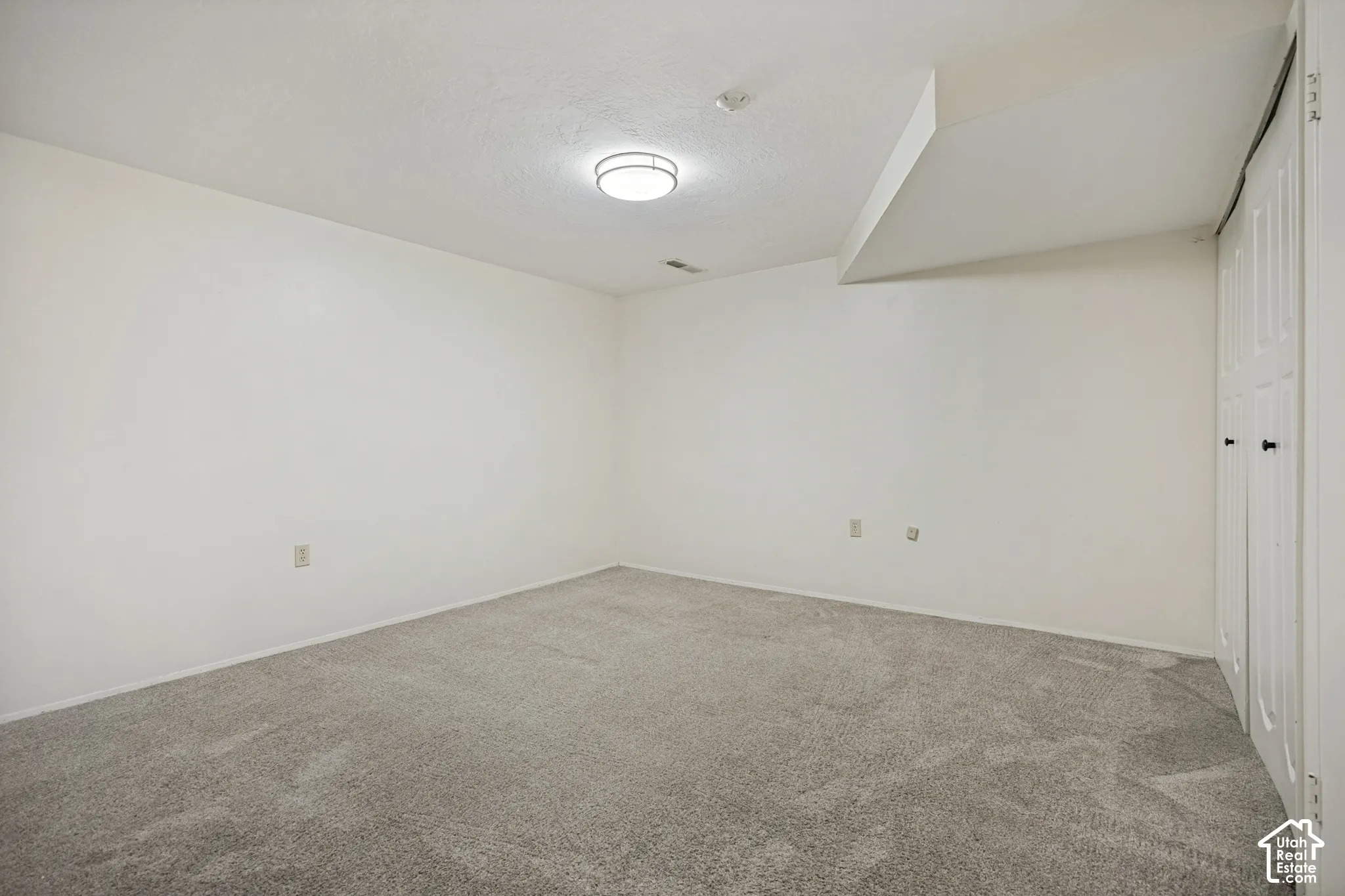 Neutral interior room featuring plush carpeting, a circular flush-mount ceiling light fixture, and double-panel closet doors