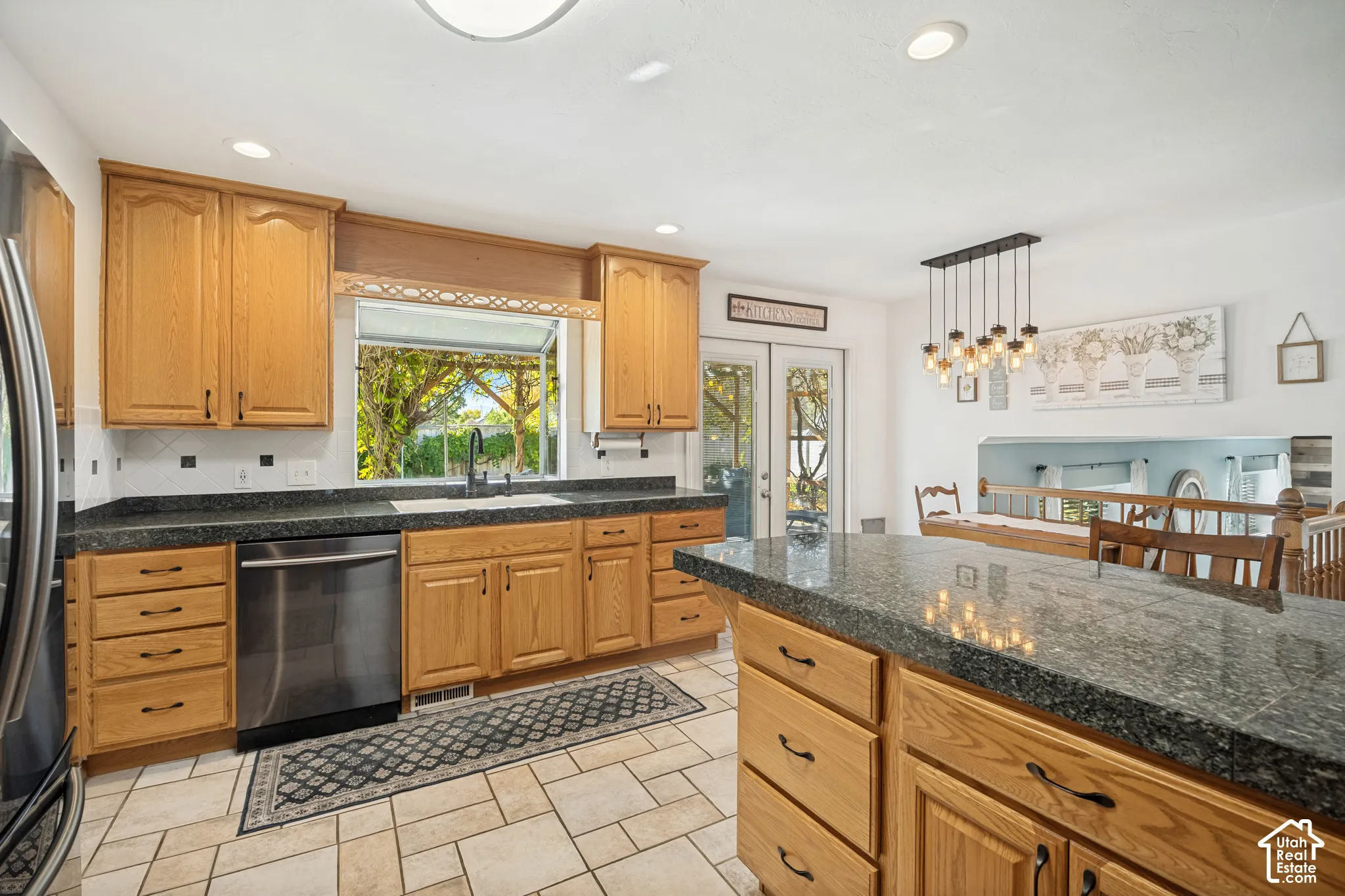 Kitchen featuring natural-finish cabinetry, stone-surface countertops, stone-tile flooring, and stainless steel dishwasher
