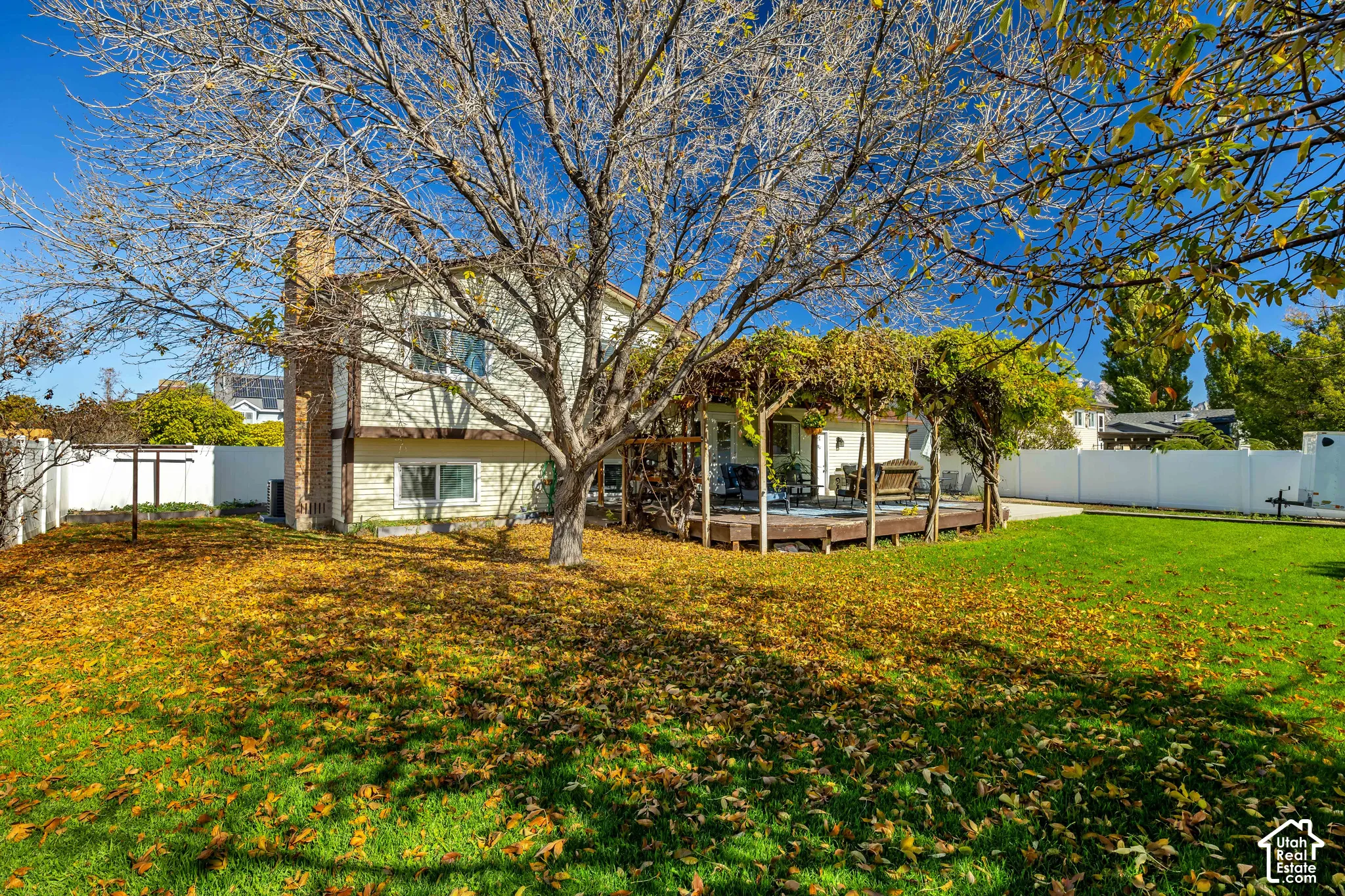 Backyard featuring a wood deck with a pergola, brick chimney, white vinyl perimeter fencing, and mature trees