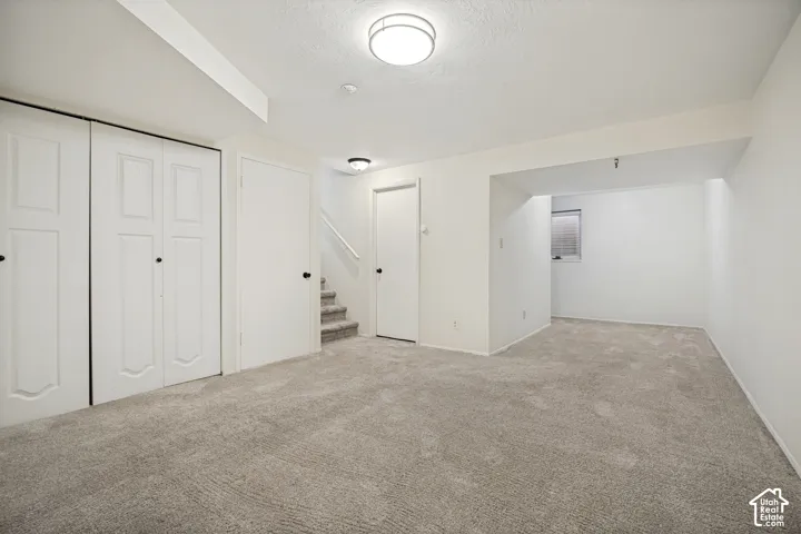 Interior space featuring neutral wall-to-wall carpeting, recessed and surface-mount flush ceiling lighting, white dual-panel closet doors, and a staircase with wall-mounted railing