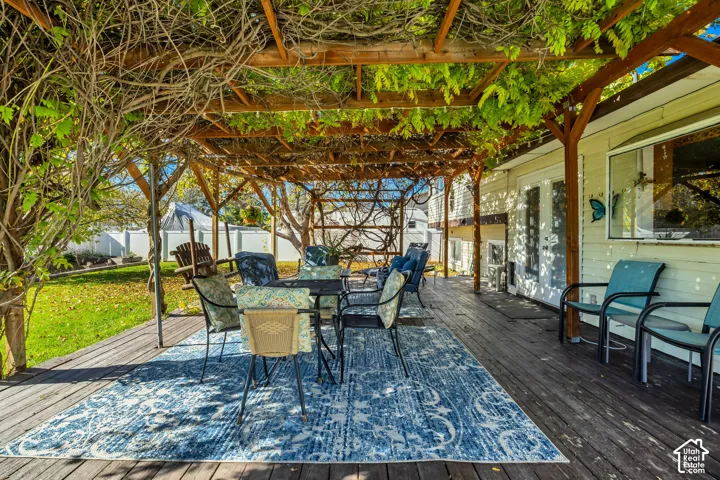 Wood-decked patio featuring a timber pergola with overhead vine growth, siding exterior, and dual glass-paneled entry doors