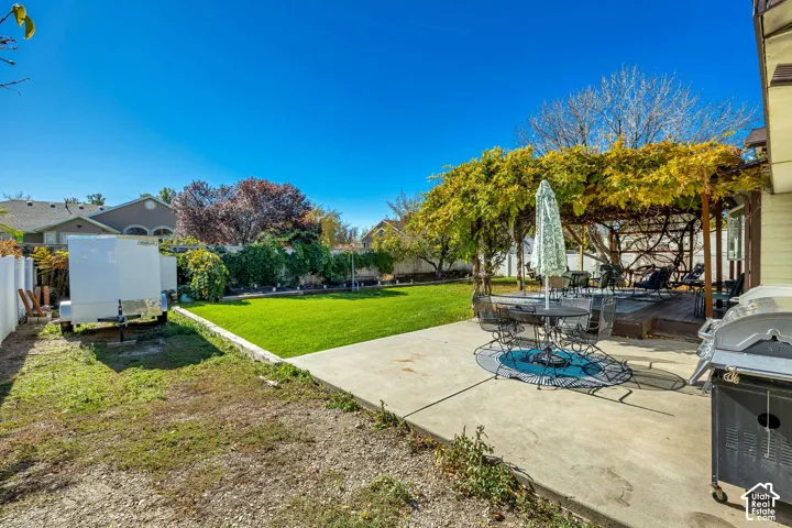 Backyard featuring a concrete patio, wood-framed pergola, manicured lawn, and perimeter privacy fencing