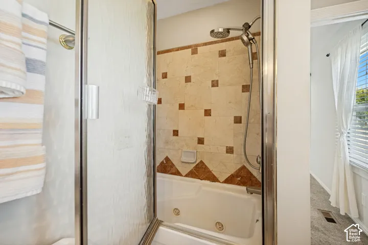 Jetted soaking tub featuring tile surround with decorative stone inlays, framed glass shower enclosure, and handheld shower fixture