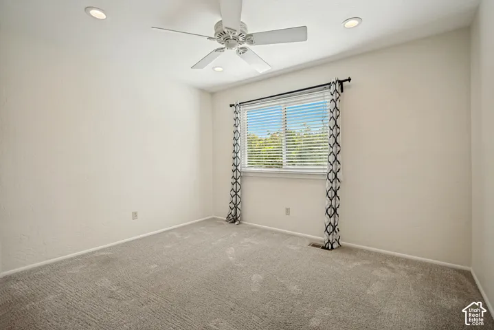 Neutral-toned carpeted room featuring a ceiling fan, recessed lighting, and a single window with blinds