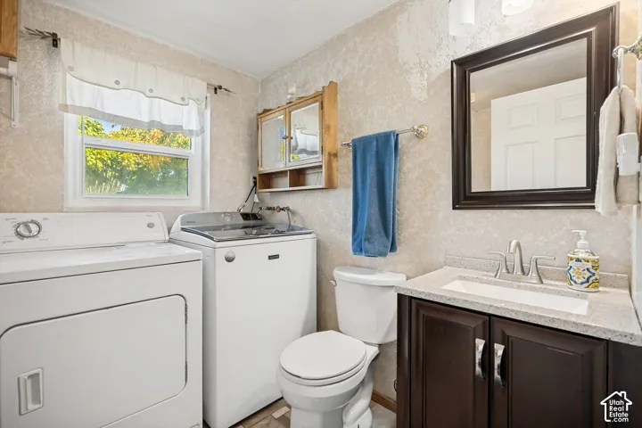 Bathroom featuring a vanity with dark-finish cabinetry, light-toned stone-finish countertop, integrated rectangular sink, and polished metal hardware, paired with a wall-mounted wooden cabinet