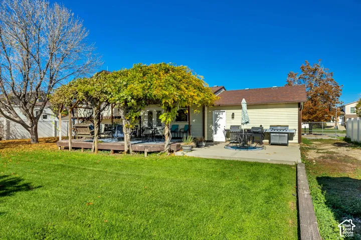 Backyard featuring a wood-decked patio with a covered pergola, a concrete patio area, and a lawn