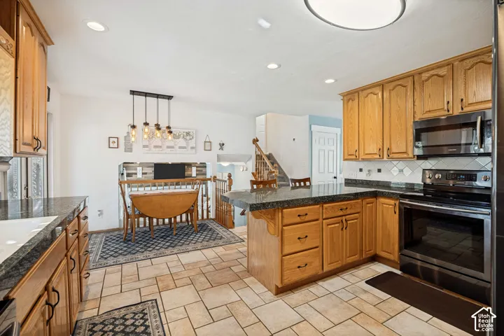 Kitchen featuring medium-tone wood cabinetry, dark stone-finish countertops, tile flooring, and integrated black kitchen appliances