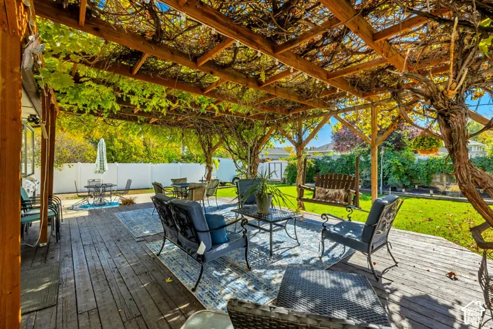 Spacious wooden deck featuring a natural wood-beam pergola with climbing vines, a manicured lawn, and a perimeter privacy fence