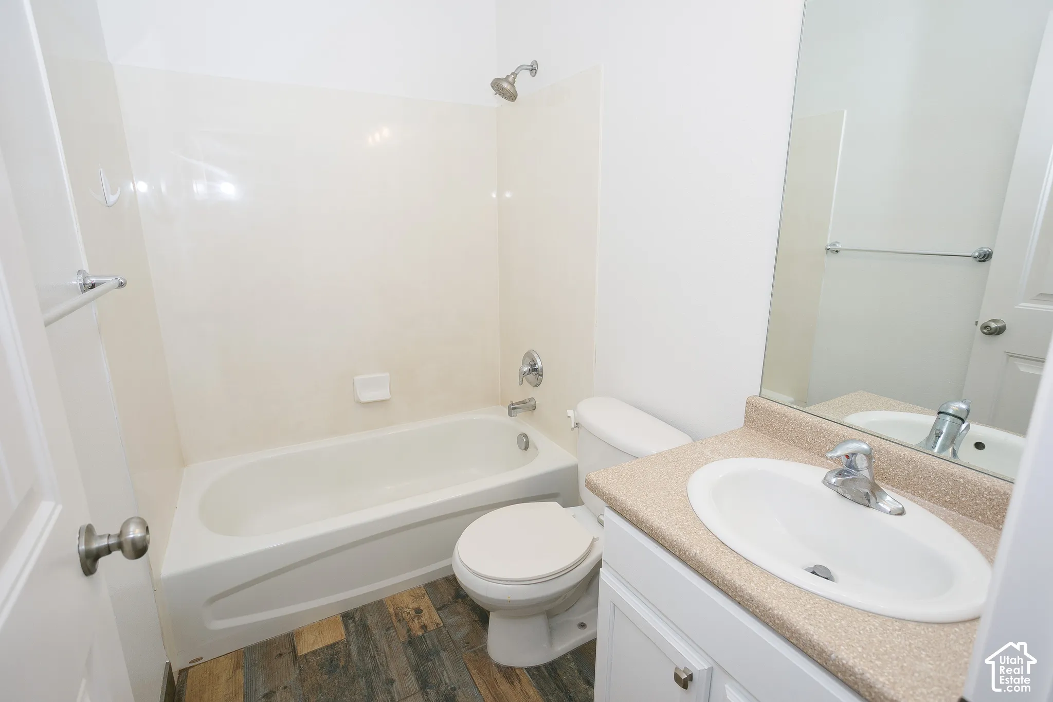Full bathroom featuring a tub-shower combination with smooth wall surrounds, a vanity with a textured countertop and integrated sink, a large wall-mounted mirror, and wood-finish flooring