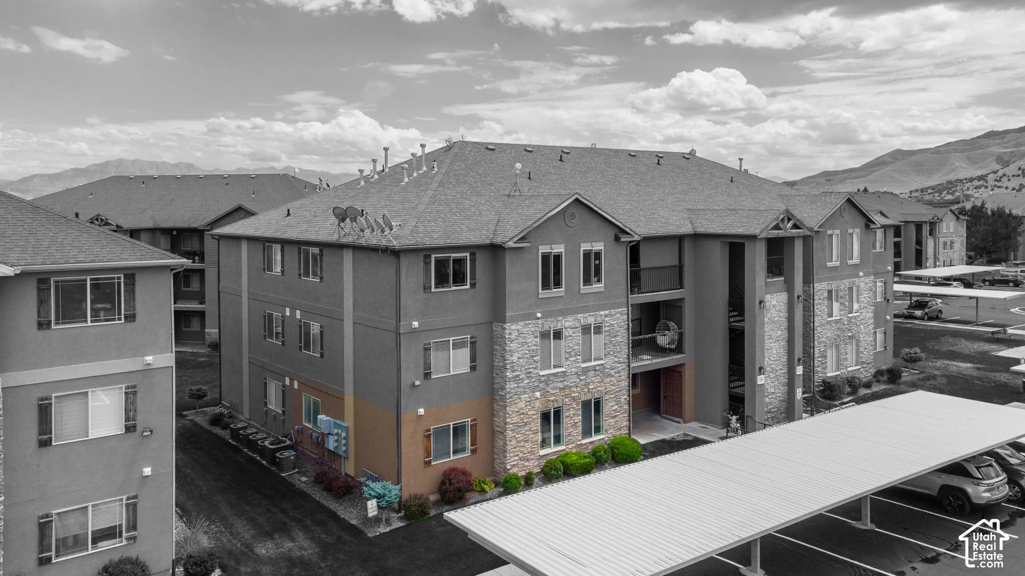 Multi-story building exterior featuring a mixed-material facade of stone veneer and stucco, asphalt shingle roofing, and integrated covered parking structures