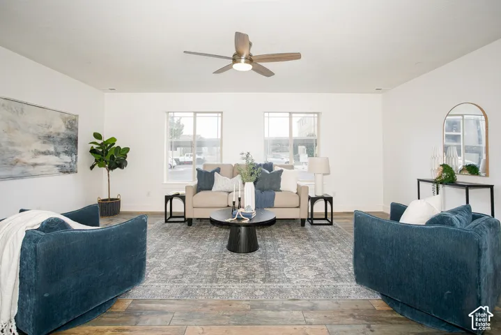 Living area featuring wood-finish flooring, two dual-pane windows, and a central ceiling fan with integrated lighting