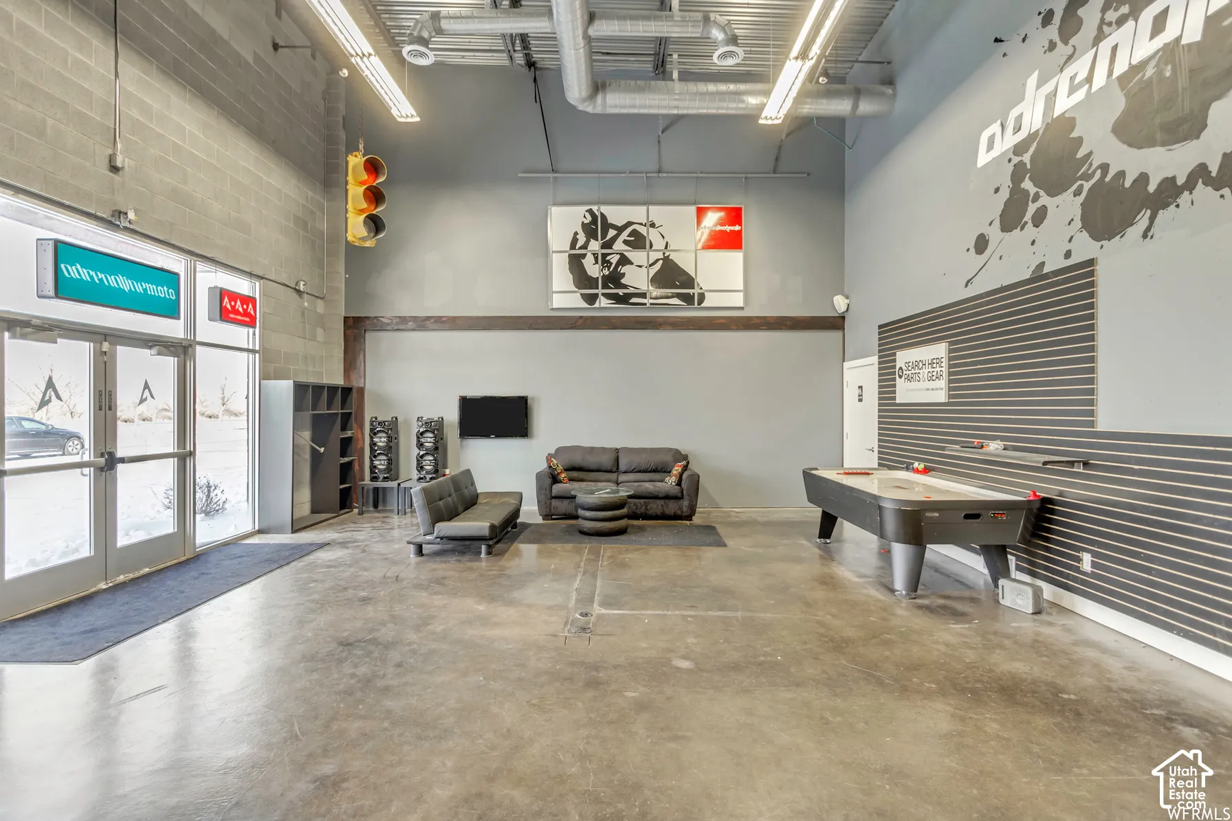 Industrial-style interior featuring high ceilings with exposed ductwork, polished concrete flooring, extensive slat wall paneling, and glass-paneled double entry doors
