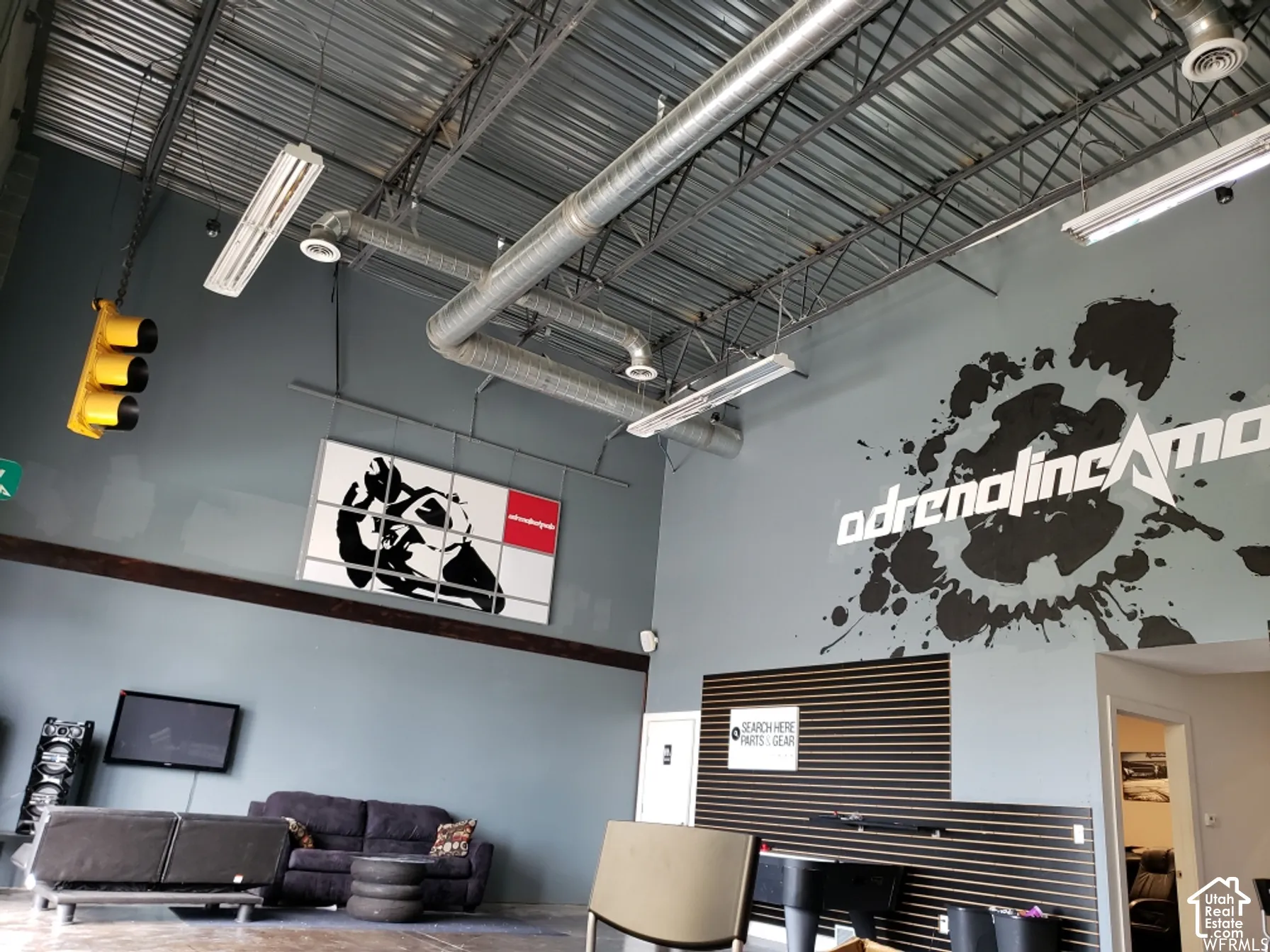 Industrial interior featuring exposed metal ceiling joists and ductwork, high-reaching walls, linear lighting fixtures, and a horizontal slat wall panel