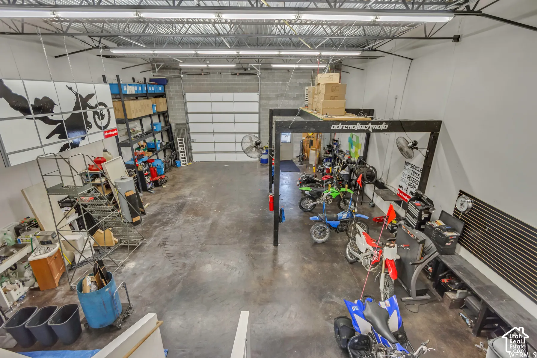 High-clearance workshop featuring concrete flooring, a large overhead roll-up door, exposed ceiling rafters, and integrated linear lighting