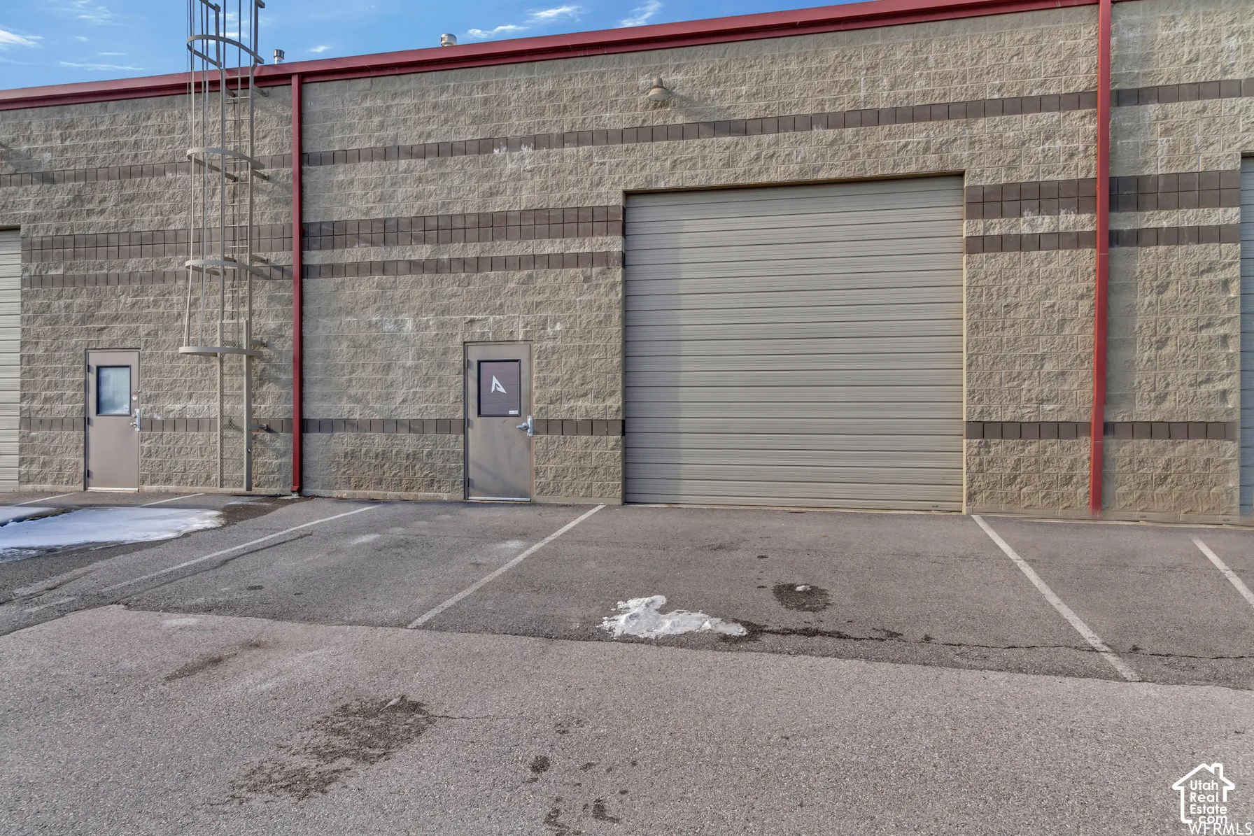 Industrial exterior featuring split-faced masonry block walls, a large roll-up bay door, a separate pedestrian entry door, and an exterior vertical access ladder