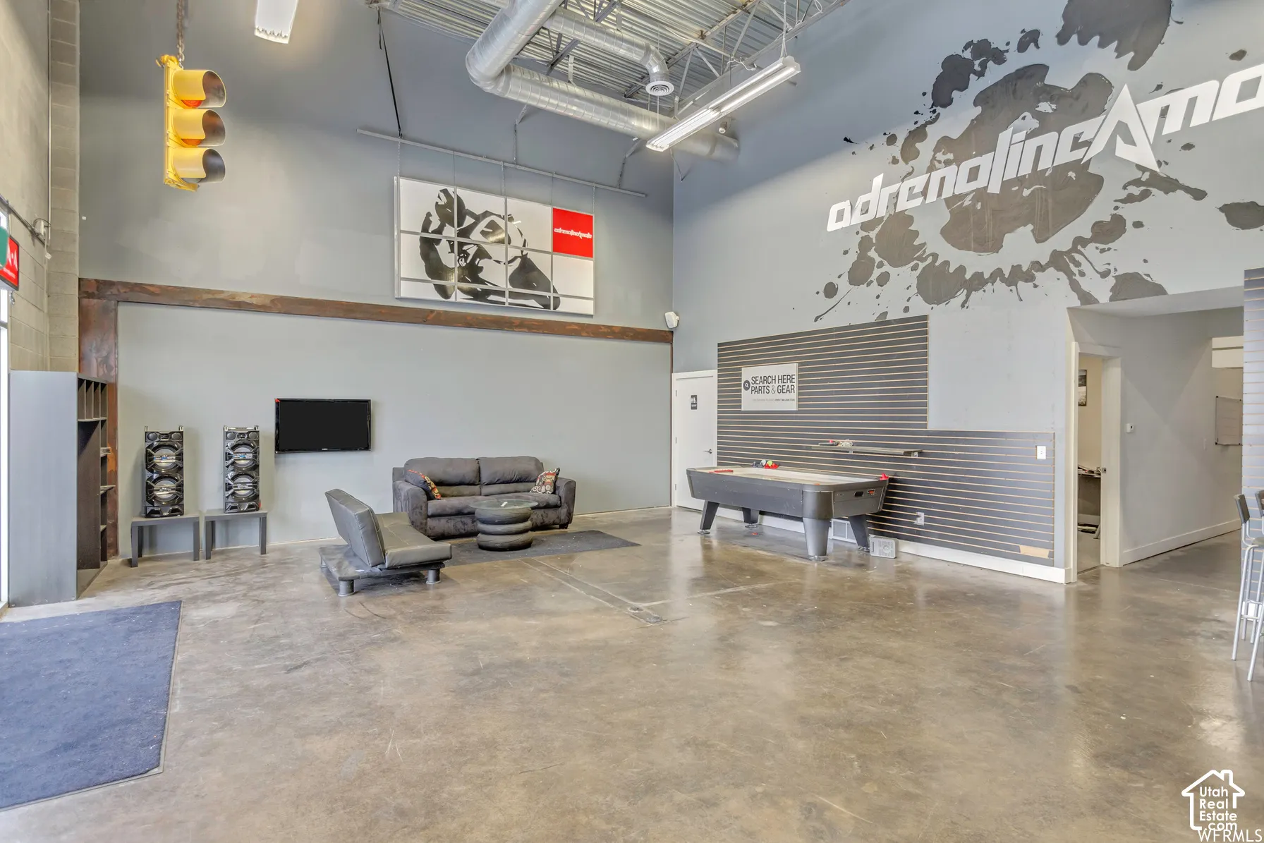 Expansive interior space featuring high ceilings with exposed ductwork, concrete flooring, corrugated metal wall paneling, and industrial-style overhead lighting