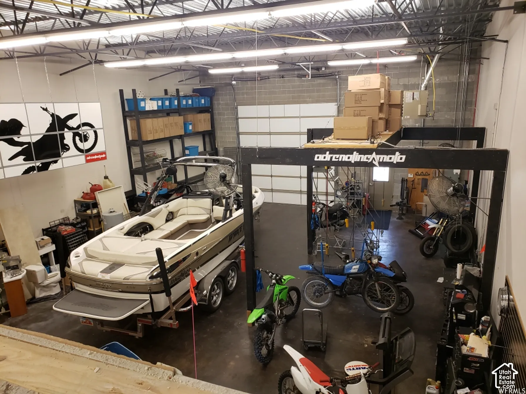 Oversized workshop featuring high ceilings with exposed structural beams, industrial-grade linear lighting, concrete masonry unit walls, and a large overhead roll-up garage door