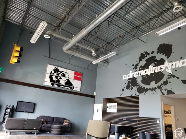 Industrial interior featuring exposed metal ceiling joists and ductwork, high-reaching walls, linear lighting fixtures, and a horizontal slat wall panel