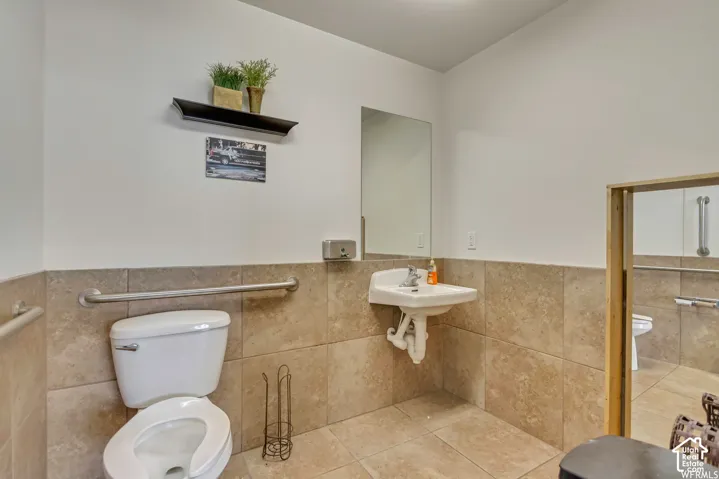 Wall-mounted sink with chrome faucet, tiled flooring, half-height wall tiling, and stainless steel grab bars
