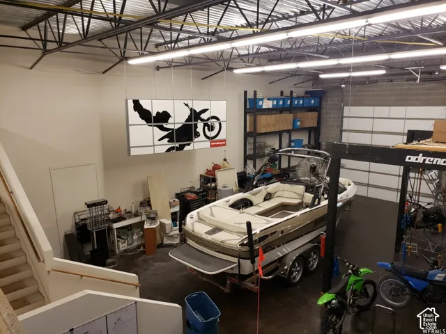 Spacious workshop featuring high ceilings with exposed trusses, concrete flooring, overhead linear lighting, and a large sectional overhead door