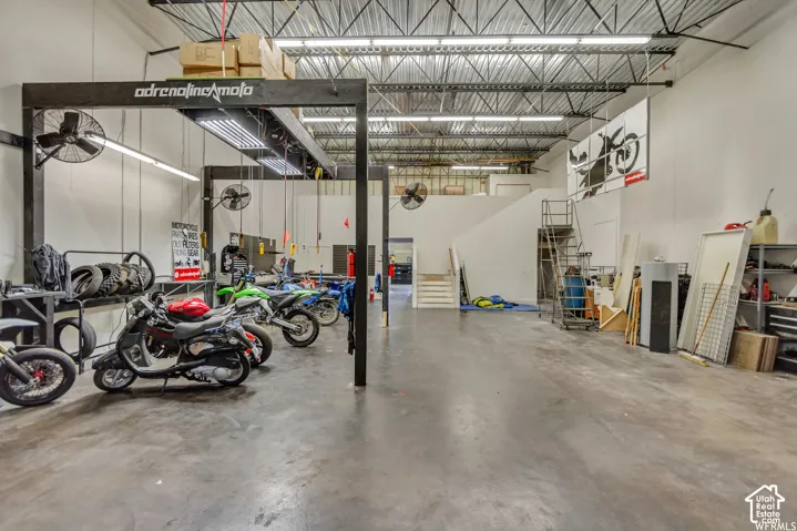 Open-concept industrial space featuring exposed metal ceiling joists, high-clearance overhead lighting, polished concrete flooring, and a steel staircase