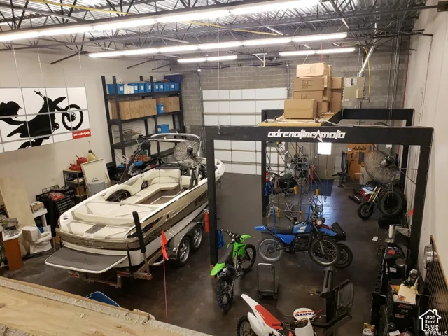Oversized workshop featuring high ceilings with exposed structural beams, industrial-grade linear lighting, concrete masonry unit walls, and a large overhead roll-up garage door