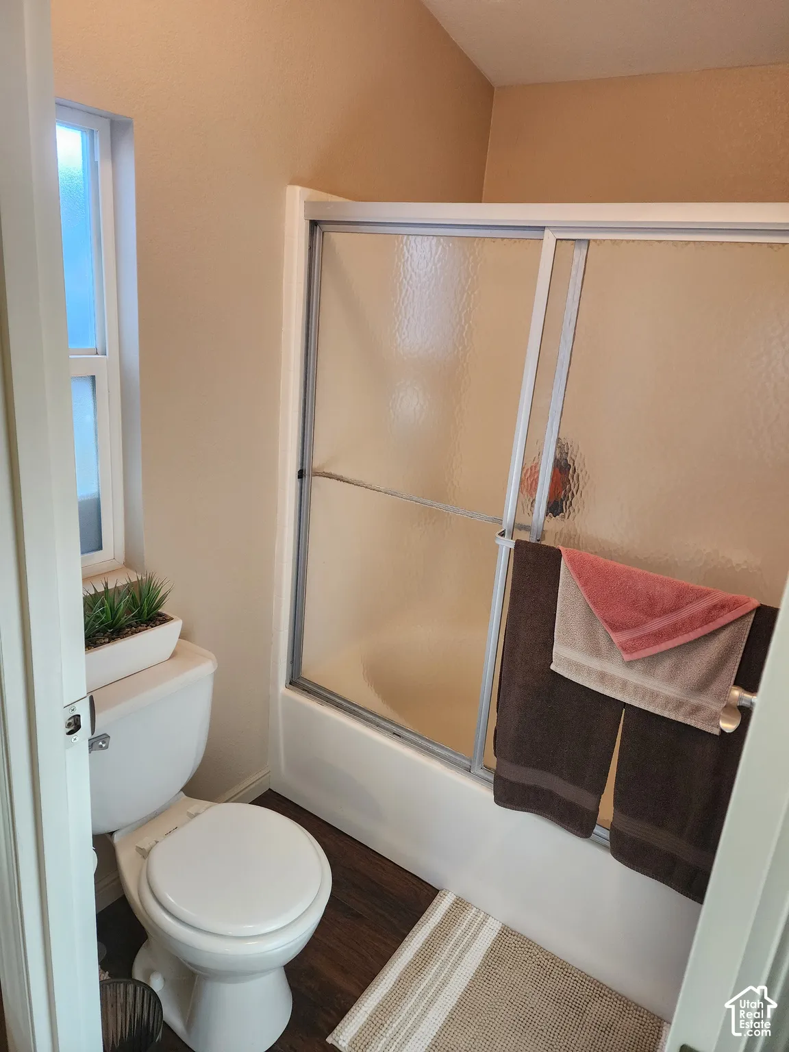 Bathroom featuring a tub-shower combination with sliding textured glass doors, wood-finish flooring, and a window providing natural light