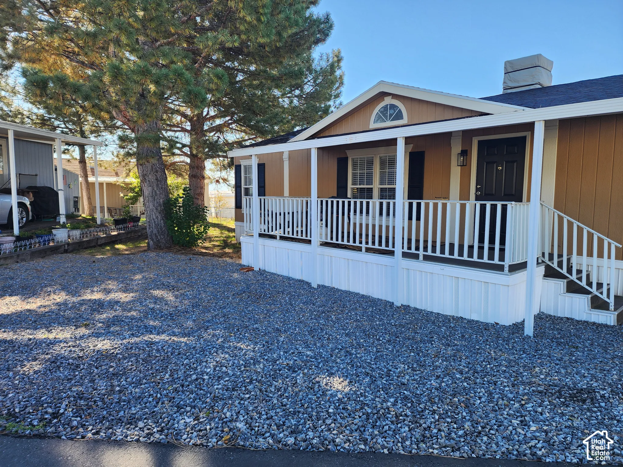 Exterior featuring a covered porch with white railing, tan siding, shutter-framed windows, and rock landscaping