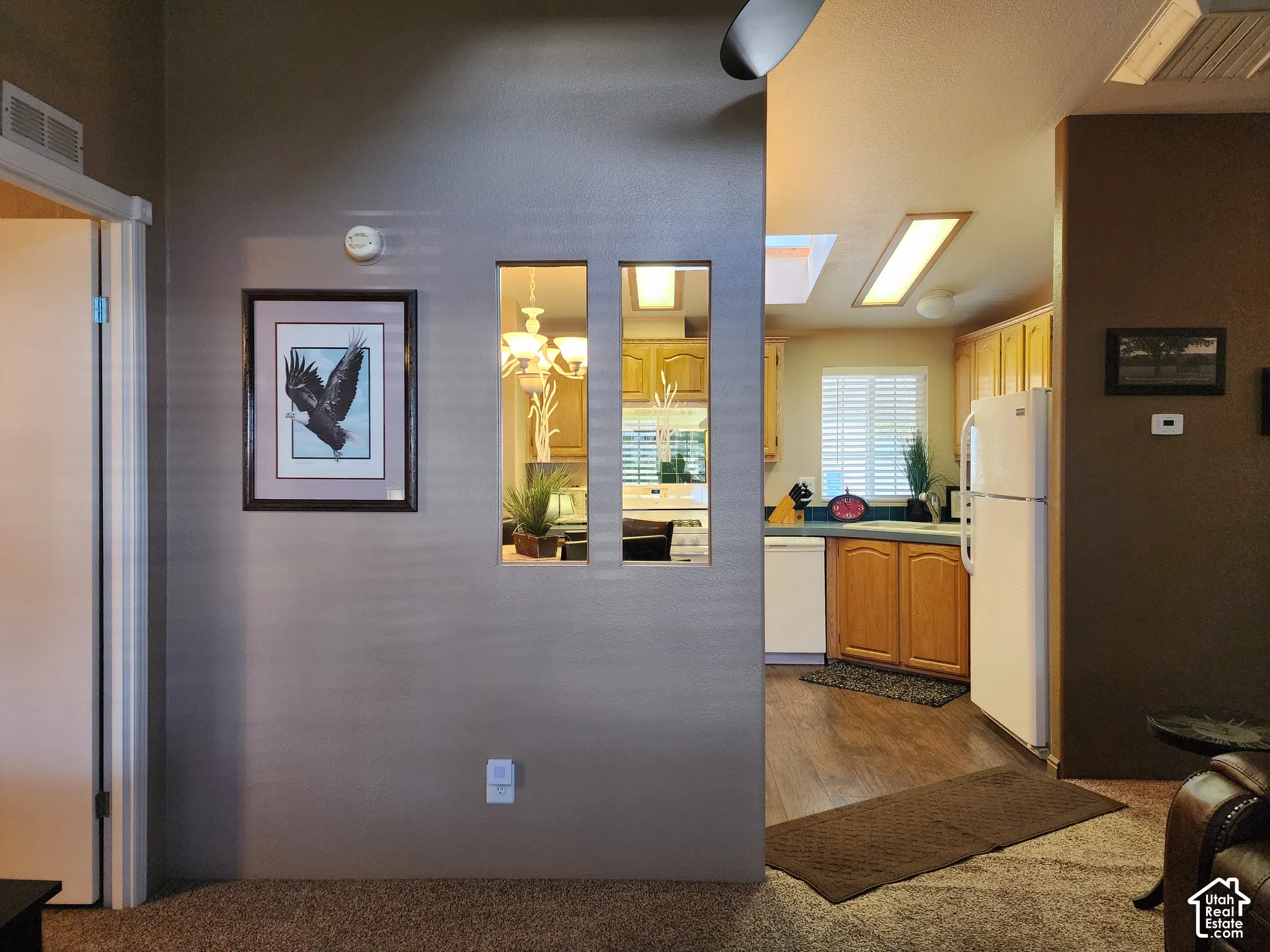 Dividing wall featuring dual vertical cutout windows, skylight, recessed lighting, wood-finish cabinetry, and white appliance suite