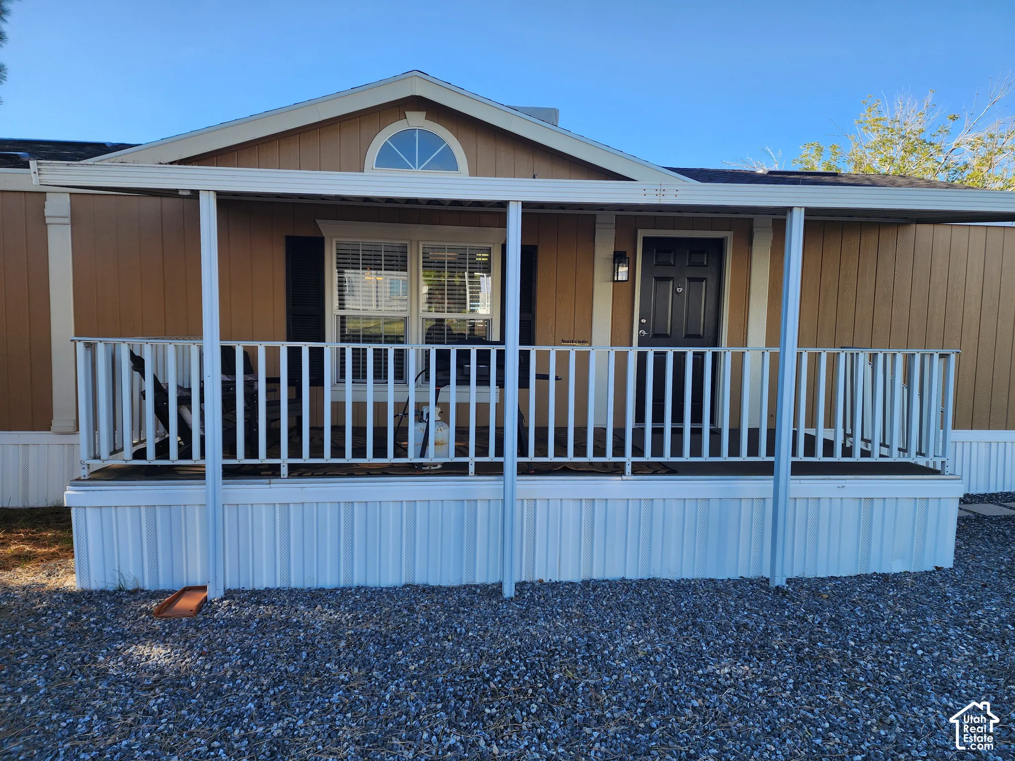 Covered front porch featuring white railing and support posts, gable roofline with decorative arched transom window, and vertical siding exterior