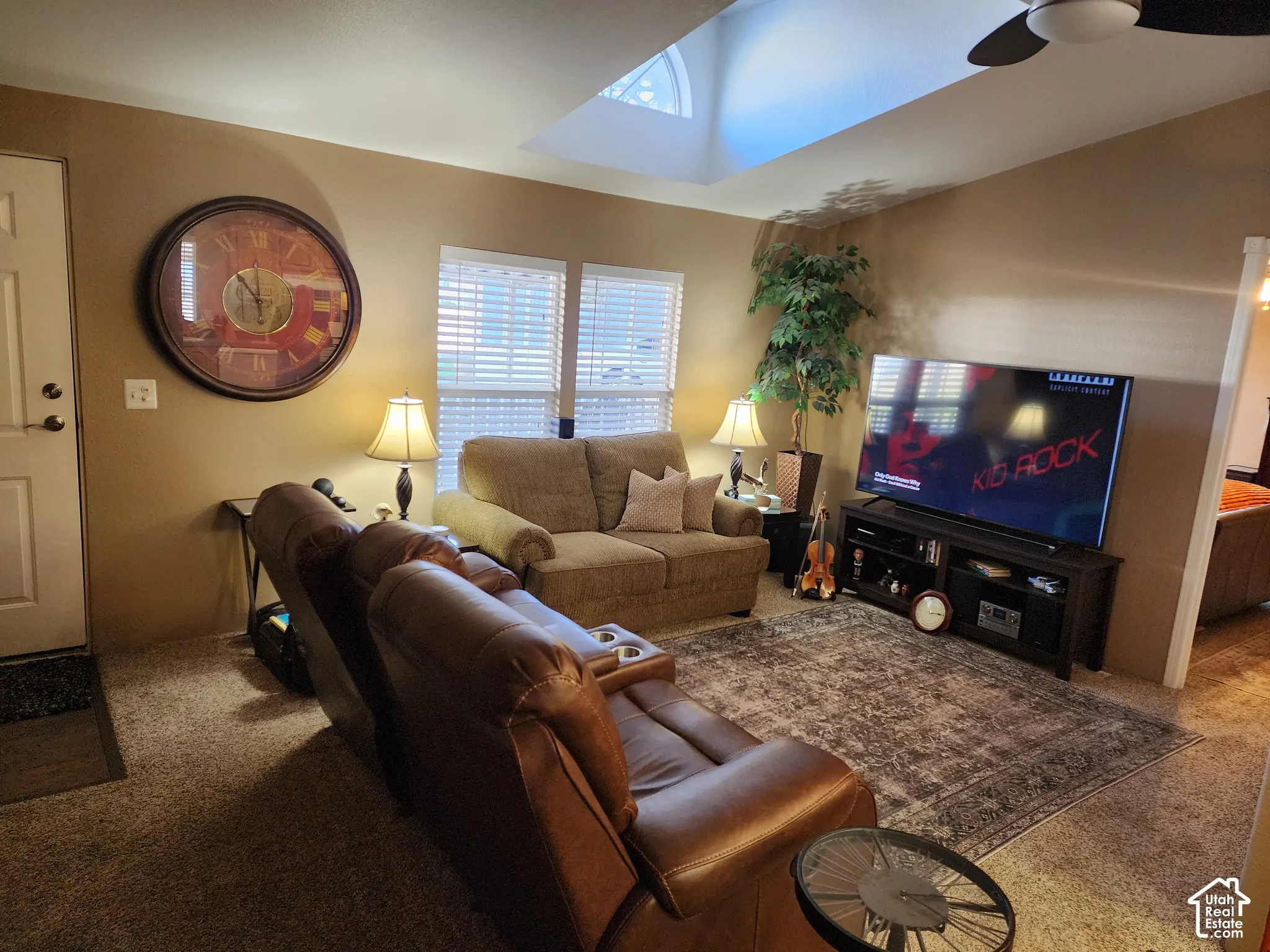 Vaulted ceiling featuring a central skylight, paired with dual-aspect windows, a ceiling fan, and carpeted flooring