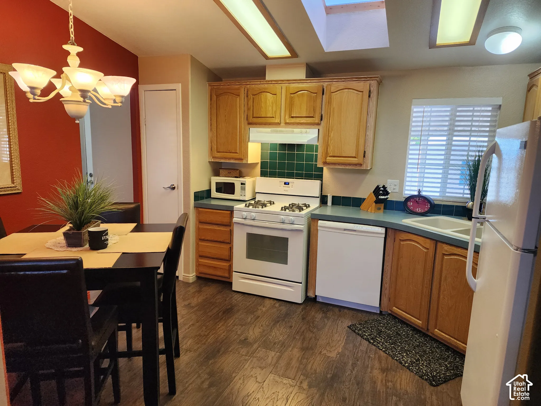 Kitchen featuring natural wood cabinetry, solid surface countertops, a tiled backsplash, wood-finish flooring, and a ceiling skylight