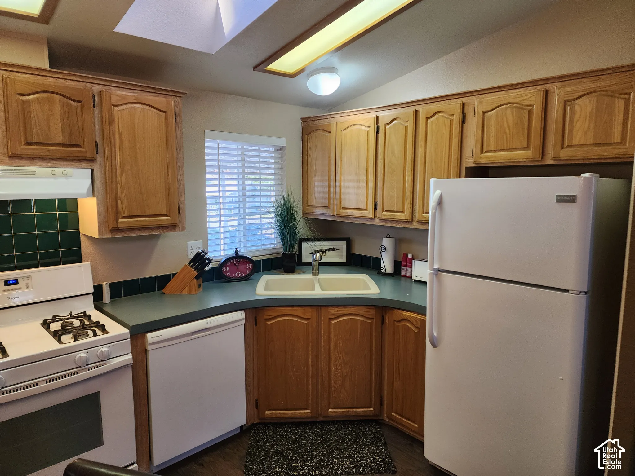 Kitchen featuring wood cabinetry, solid-surface countertops, dual-basin sink, and recessed ceiling lighting