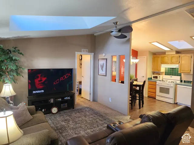 Vaulted ceilings featuring multiple skylights, kitchen with wooden cabinetry, and interior pass-through window with paneled wall