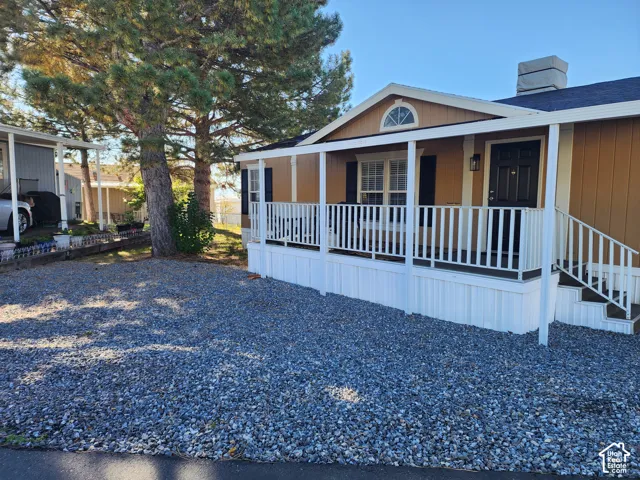 Exterior featuring a covered porch with white railing, tan siding, shutter-framed windows, and rock landscaping