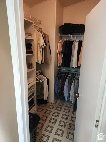 Reach-in closet featuring white built-in shelving, multi-level hanging rods, and patterned tile flooring