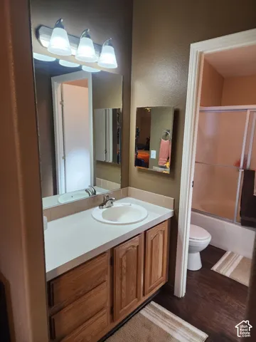 Bathroom vanity featuring a solid surface countertop, integrated oval basin, polished metal faucet, wood-finish cabinetry, and a tri-light wall-mounted fixture