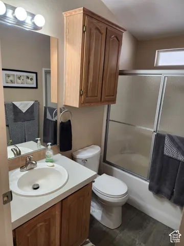 Bathroom featuring a wood-finish vanity with a molded countertop, mounted wood cabinetry, a sliding glass door shower enclosure, and wood-finish flooring