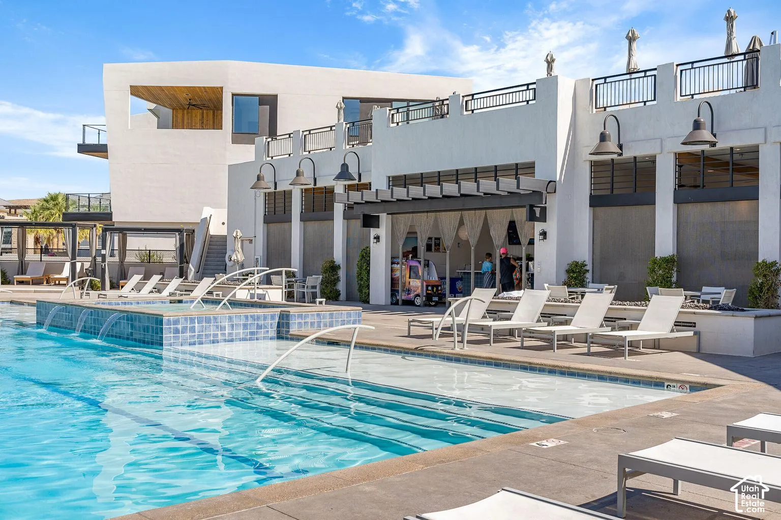 Swimming pool featuring a raised tiled spillway, integrated entry steps, and an expansive concrete pool deck with built-in perimeter lighting and a covered patio structure