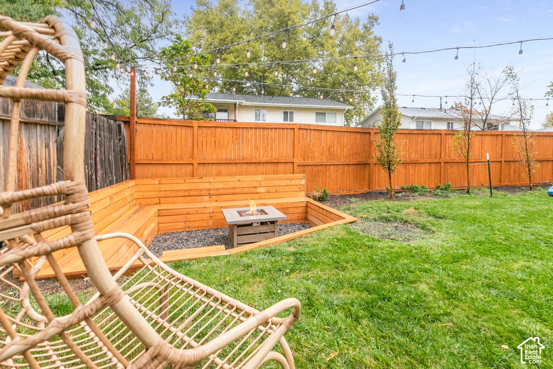 Backyard featuring a wood privacy fence, integrated wood bench seating, a stone-surround fire pit, and overhead string lighting